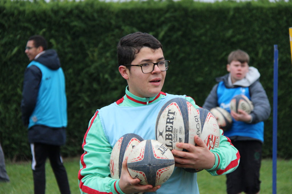Un jeune garçon rapporte 4 ballons de rugby à la fin de l'exercice.
