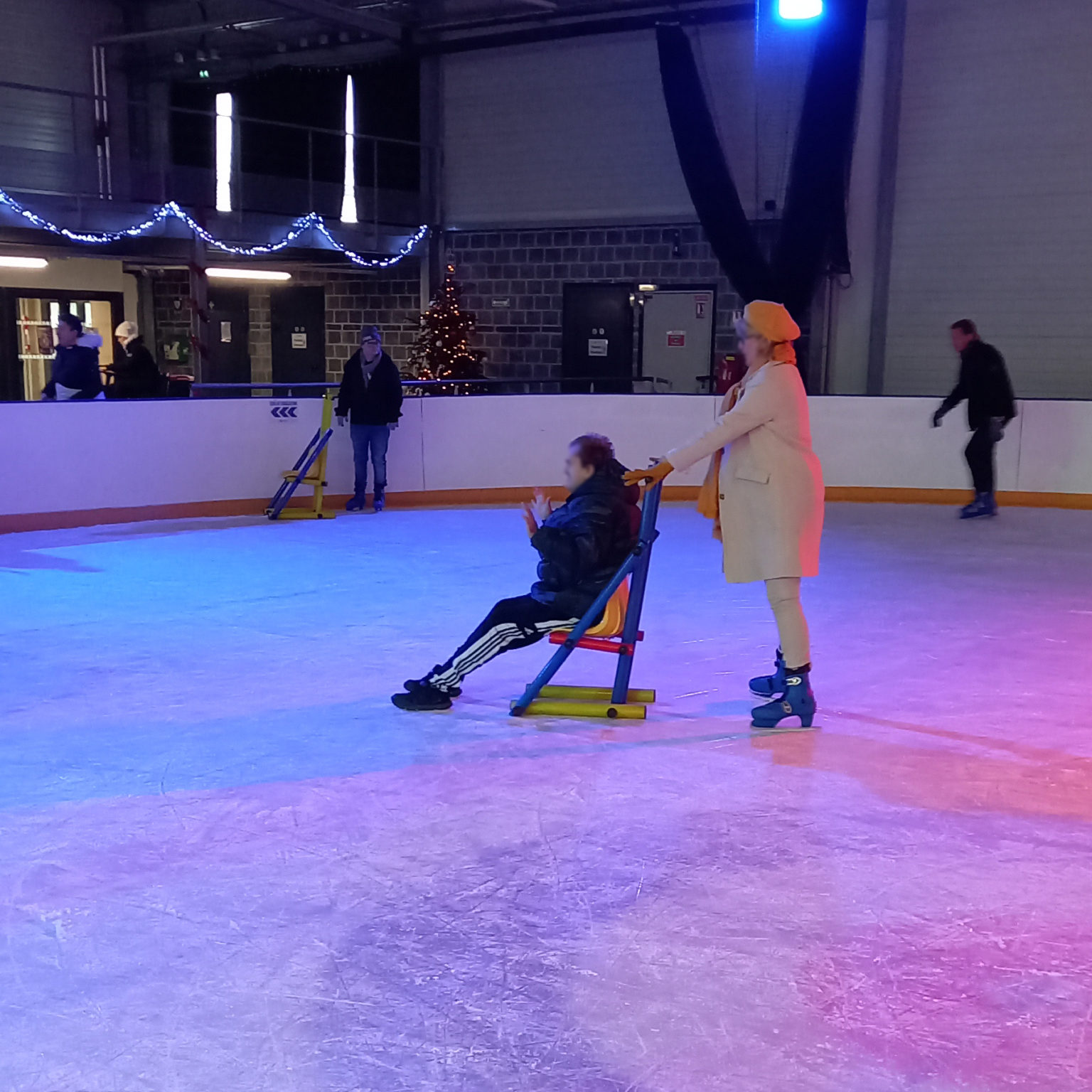 Une professionnelle pousse un résident sur la patinoire avec une chaise adaptée.