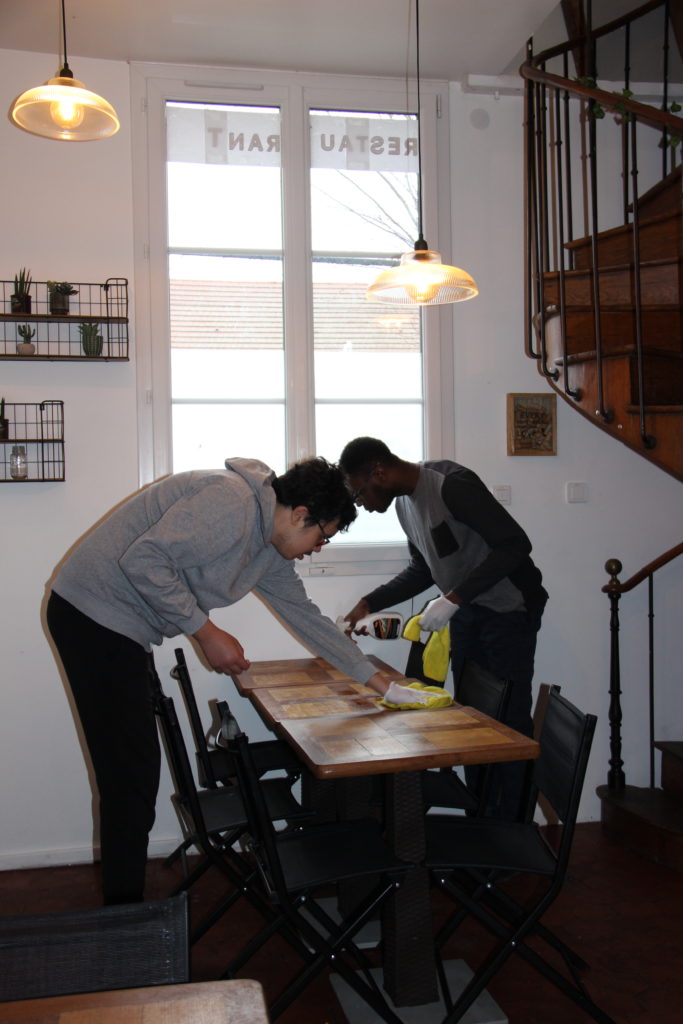 Joshua et Yanis nettoient les tables de l'espace restauration de l'épicerie solidaire, dans le cadre d'un projet d'inclusion.