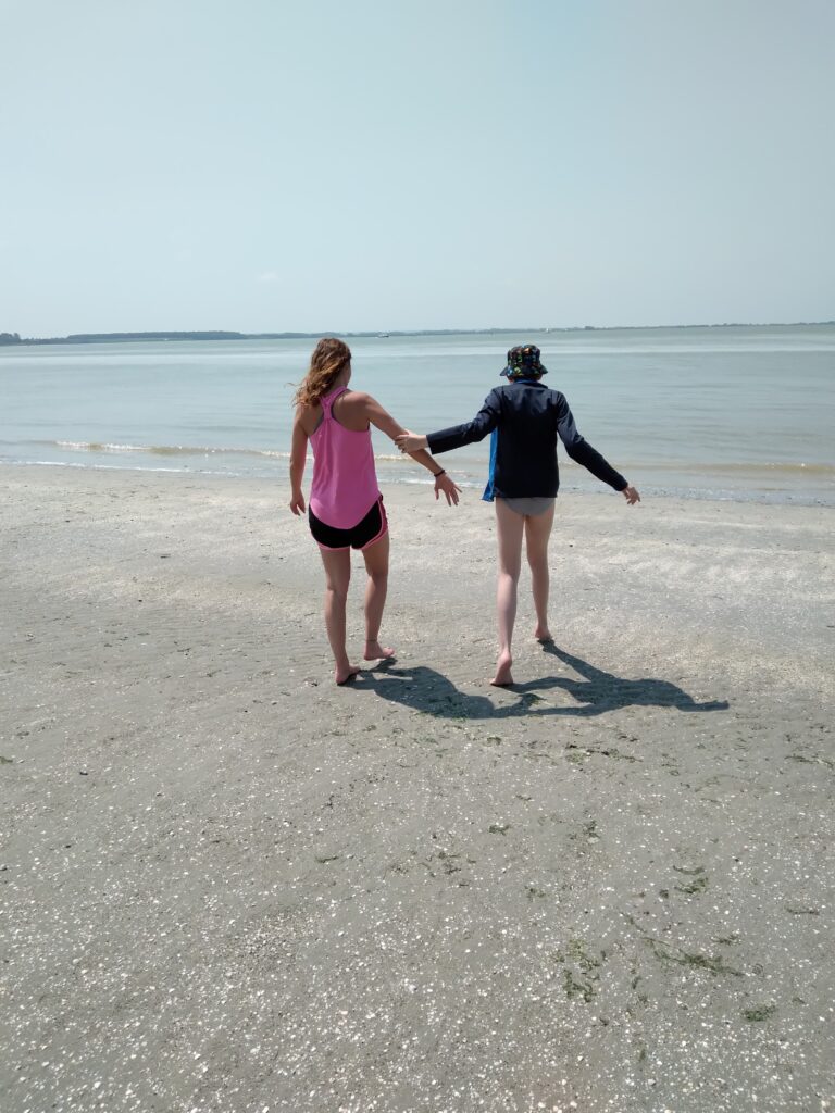 Un jeune et une éducatrice, sur la plage, se dirigent vers la mer pour se tremper les pieds.