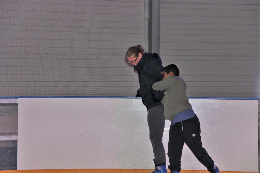 Un jeune garçon découvre le patinage sur glace à l'aide de son éducatrice